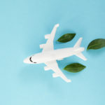 White airplane model emitting fresh green leaves on blue background. Sustainable travel; clean and green energy; and biofuel for aviation industry concept