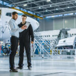 Business aviation Aircraft Maintenance Worker and Engineer having Conversation. Holding Tablet.